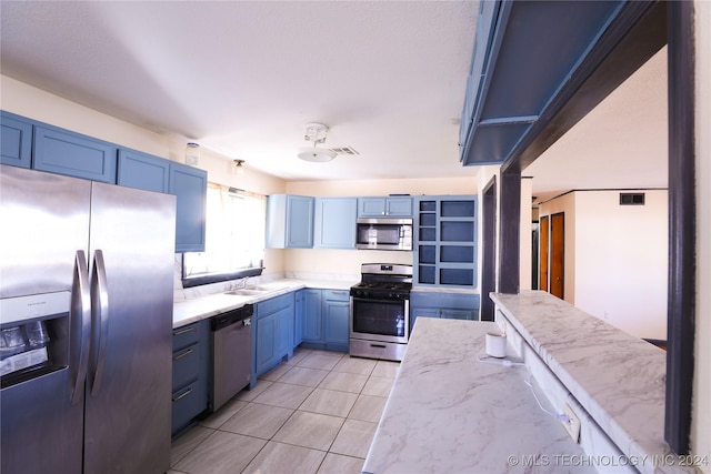 kitchen with light stone countertops, sink, blue cabinets, and stainless steel appliances