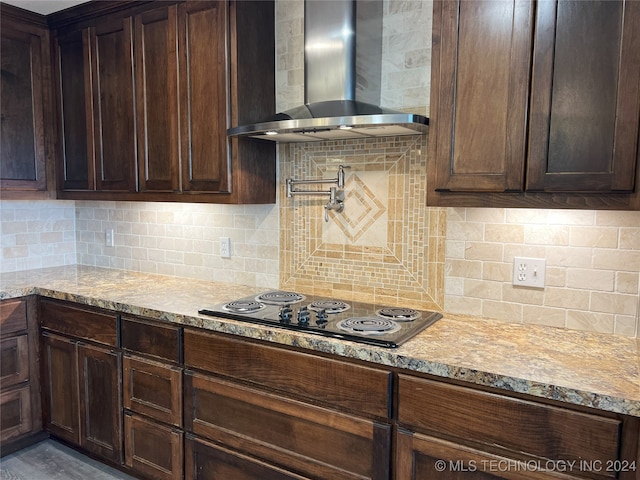 kitchen featuring wall chimney range hood, light stone countertops, tasteful backsplash, dark brown cabinetry, and electric stovetop