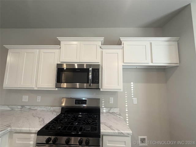 kitchen with light stone countertops, appliances with stainless steel finishes, and white cabinetry