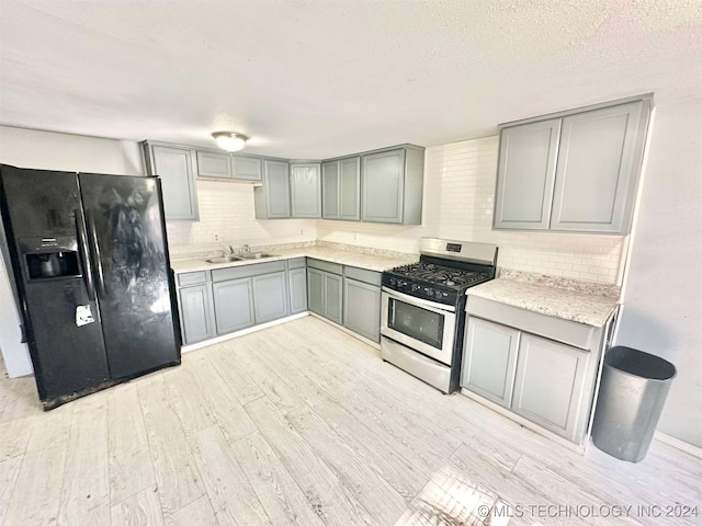 kitchen with stainless steel gas range oven, black refrigerator with ice dispenser, gray cabinets, tasteful backsplash, and light hardwood / wood-style floors