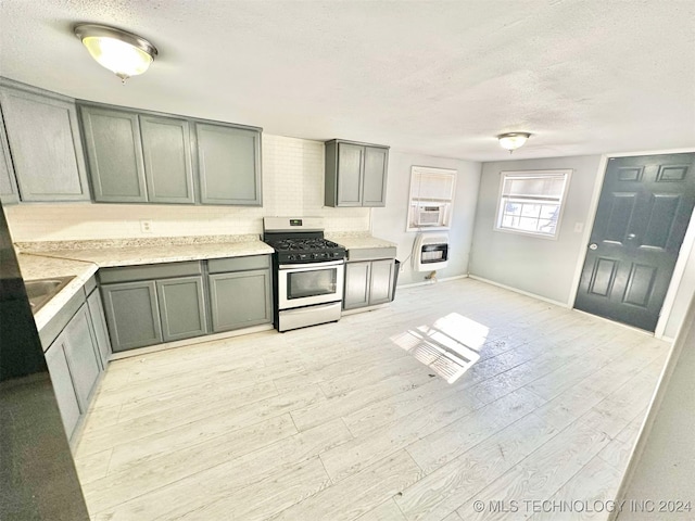 kitchen with light wood-type flooring, gas range oven, a textured ceiling, and heating unit