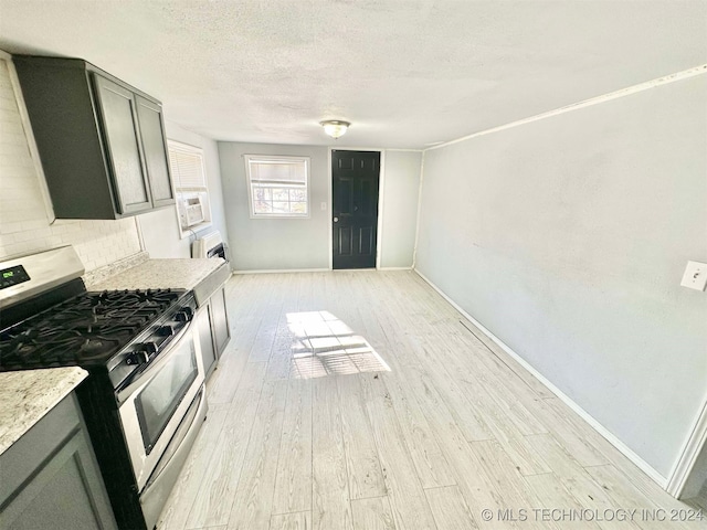 kitchen with stainless steel gas range oven, light stone countertops, a textured ceiling, tasteful backsplash, and light hardwood / wood-style floors