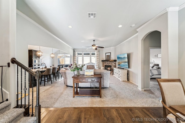 living room with ceiling fan with notable chandelier, carpet floors, a brick fireplace, and ornamental molding