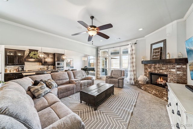 carpeted living room featuring ceiling fan with notable chandelier, a brick fireplace, and crown molding