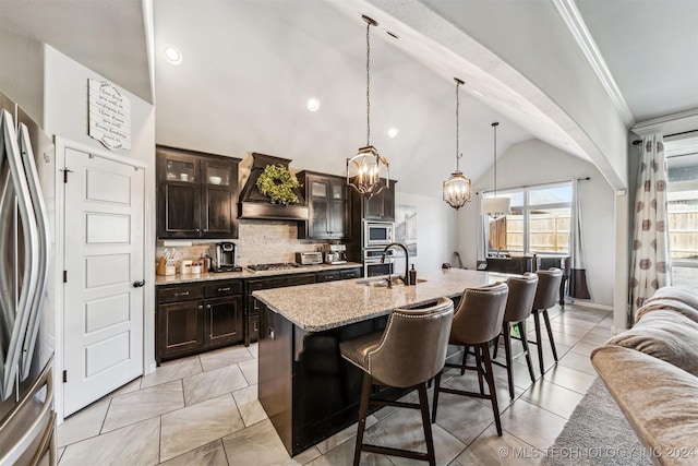 kitchen with premium range hood, vaulted ceiling, a kitchen island with sink, dark brown cabinets, and appliances with stainless steel finishes