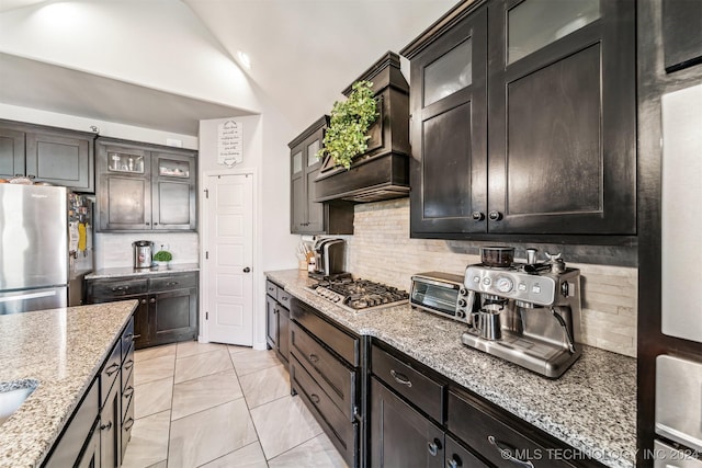 kitchen with dark brown cabinetry, stainless steel appliances, light stone counters, decorative backsplash, and custom exhaust hood