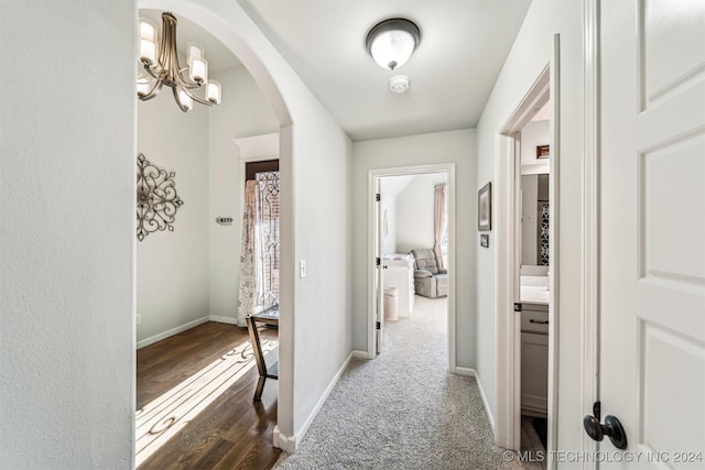 hall featuring dark colored carpet and an inviting chandelier