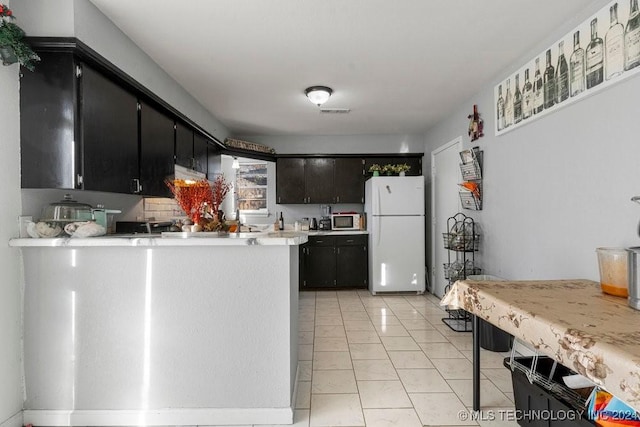 kitchen with kitchen peninsula, white fridge, and light tile patterned floors