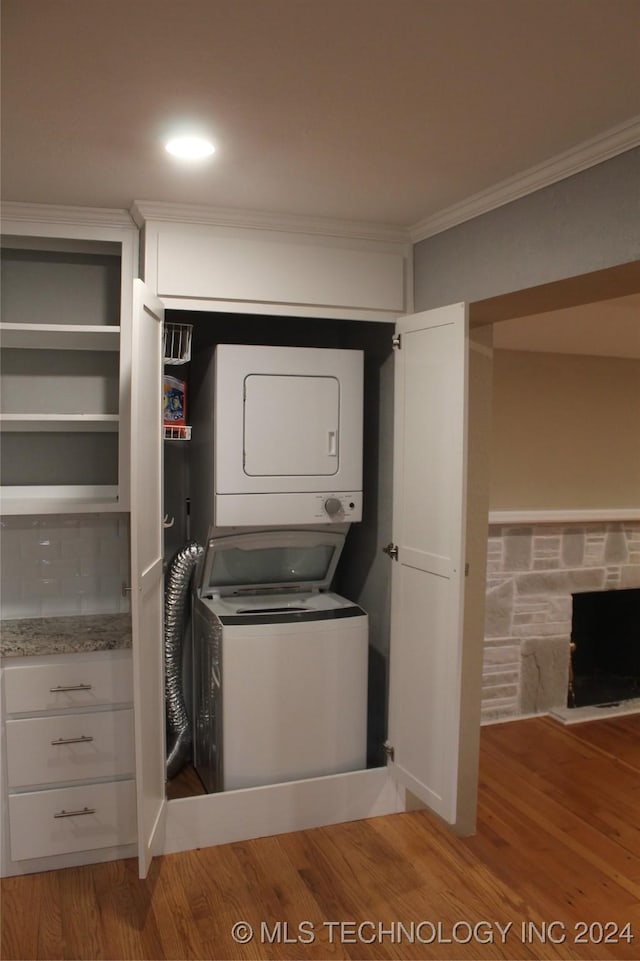 clothes washing area with a stone fireplace, wood-type flooring, and stacked washer / dryer