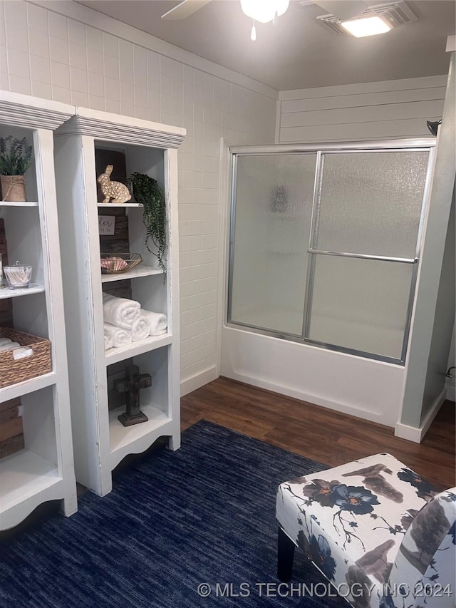 bathroom with hardwood / wood-style flooring, wood walls, and shower / bath combination with glass door