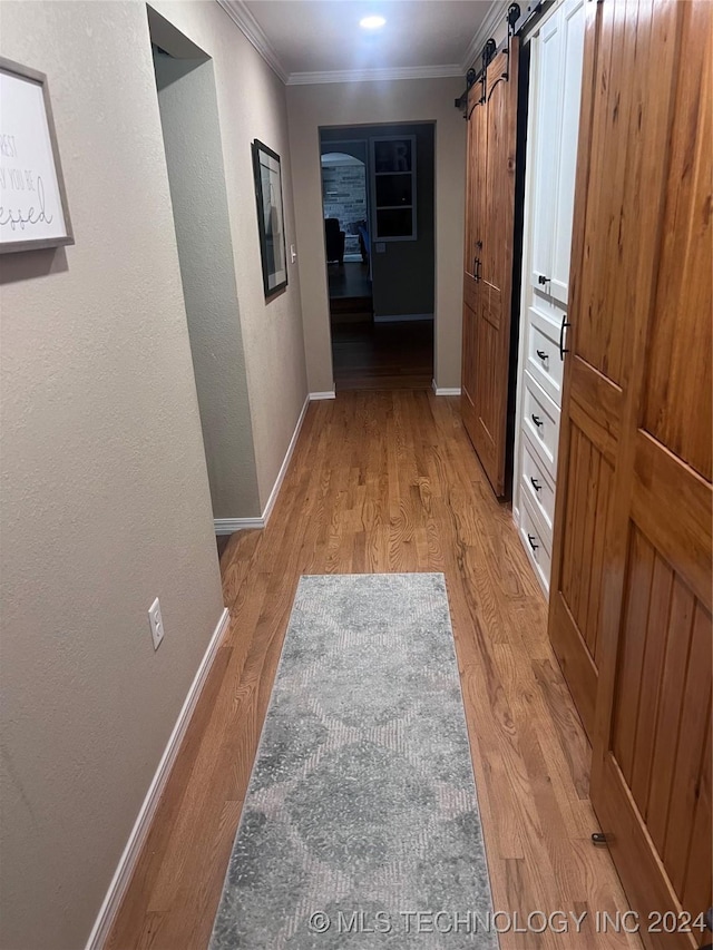 hallway featuring a barn door, light hardwood / wood-style flooring, and crown molding