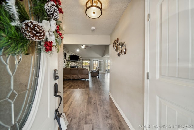 entryway with a stone fireplace, wood-type flooring, a textured ceiling, and vaulted ceiling