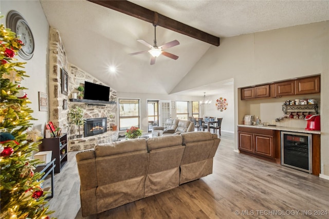 living room featuring ceiling fan with notable chandelier, light hardwood / wood-style flooring, a fireplace, a textured ceiling, and beverage cooler