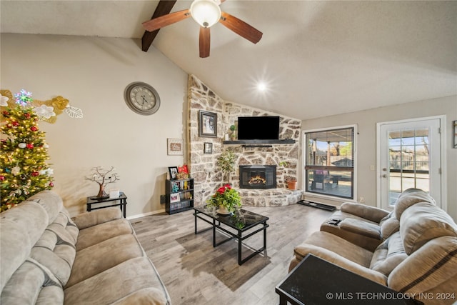 living room featuring vaulted ceiling with beams, light hardwood / wood-style flooring, ceiling fan, and a stone fireplace