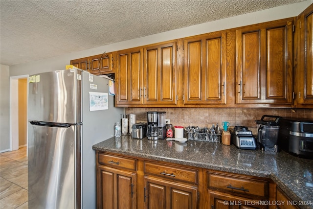 kitchen featuring backsplash, stainless steel fridge, dark stone counters, a textured ceiling, and light tile patterned flooring