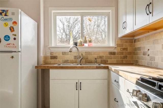 kitchen with decorative backsplash, stove, sink, white cabinets, and white fridge