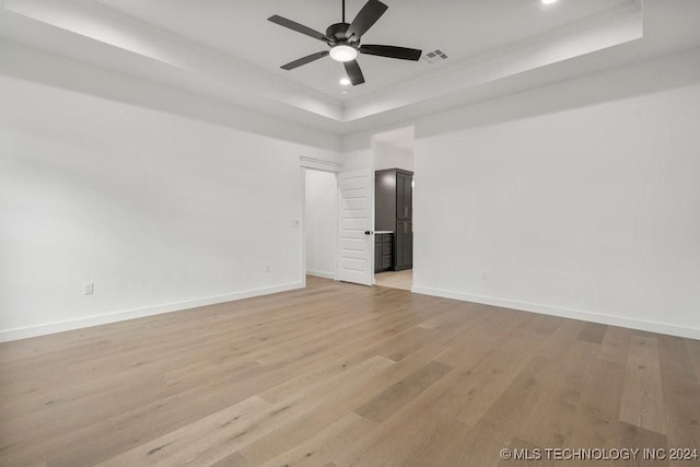 spare room with a tray ceiling, ceiling fan, and light hardwood / wood-style floors