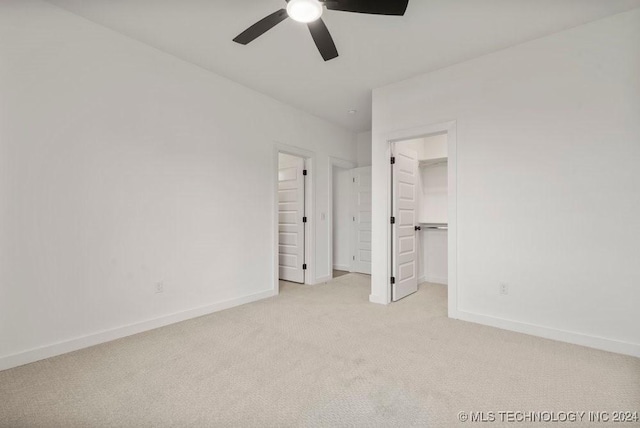 unfurnished bedroom with light carpet, a walk in closet, a closet, and ceiling fan