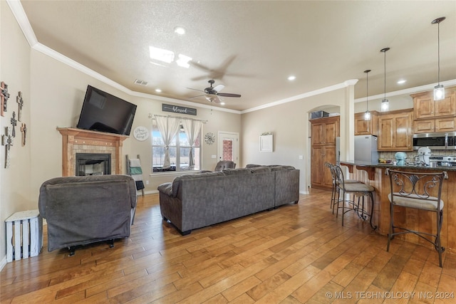 living room with hardwood / wood-style flooring, ceiling fan, ornamental molding, and a tiled fireplace