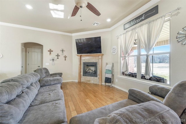 living room with a tile fireplace, ceiling fan, ornamental molding, and hardwood / wood-style flooring