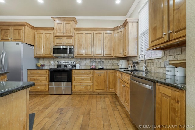 kitchen with sink, light hardwood / wood-style flooring, dark stone counters, appliances with stainless steel finishes, and ornamental molding