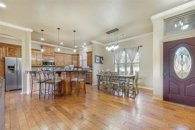 kitchen with hanging light fixtures, a kitchen breakfast bar, light hardwood / wood-style floors, appliances with stainless steel finishes, and ornamental molding