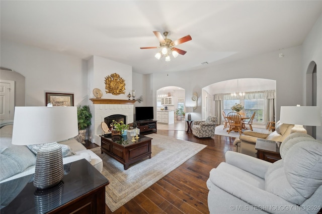 living room with ceiling fan with notable chandelier, dark hardwood / wood-style floors, and a brick fireplace