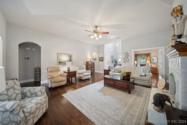 living room featuring a fireplace, ceiling fan, and dark wood-type flooring