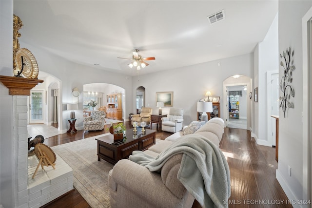 living room featuring ceiling fan, dark wood-type flooring, and a brick fireplace