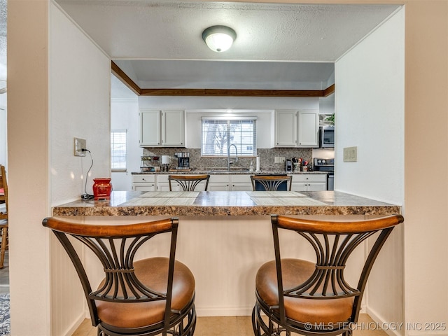 kitchen featuring a breakfast bar, white cabinetry, kitchen peninsula, and appliances with stainless steel finishes