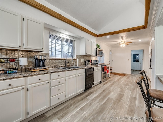 kitchen with dark stone counters, stainless steel appliances, vaulted ceiling, sink, and white cabinetry