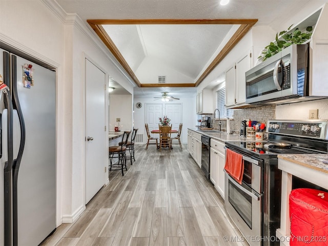 kitchen with ceiling fan, sink, stainless steel appliances, vaulted ceiling, and white cabinets