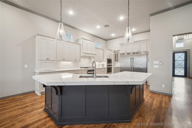 kitchen with tasteful backsplash, white cabinetry, sink, built in refrigerator, and a large island