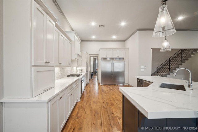 kitchen with sink, white cabinetry, hanging light fixtures, a large island with sink, and stainless steel built in fridge