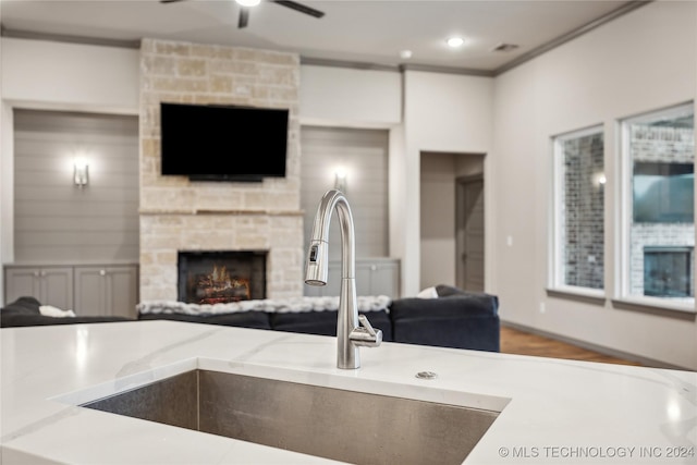 kitchen with crown molding, sink, a stone fireplace, and ceiling fan