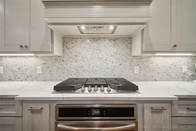 kitchen with tasteful backsplash, light stone countertops, premium range hood, and stainless steel appliances