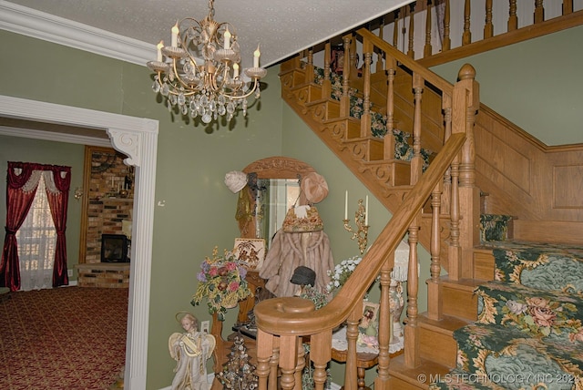 stairs featuring a textured ceiling, a large fireplace, ornamental molding, and a notable chandelier