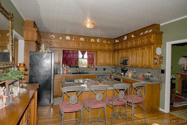 kitchen with sink, light wood-type flooring, a kitchen bar, black microwave, and stainless steel refrigerator