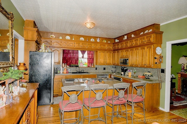 kitchen featuring sink, light hardwood / wood-style flooring, fridge, a kitchen bar, and black microwave