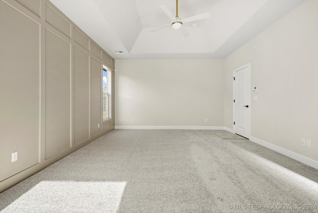 unfurnished room featuring ceiling fan, light carpet, and a tray ceiling