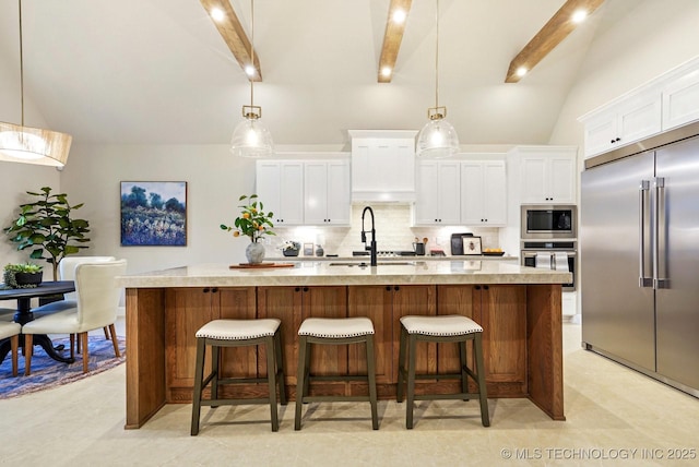 kitchen featuring white cabinets, decorative light fixtures, built in appliances, decorative backsplash, and a center island with sink