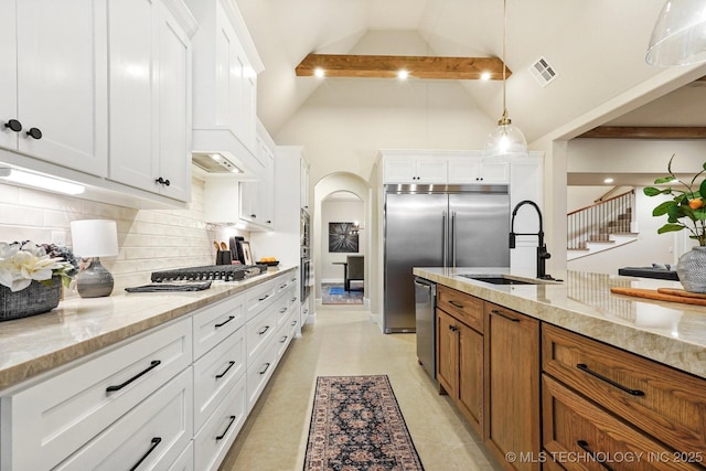 kitchen featuring pendant lighting, beam ceiling, sink, light stone countertops, and white cabinets