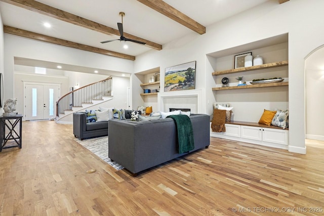 living room featuring ceiling fan, built in features, beamed ceiling, and light hardwood / wood-style floors