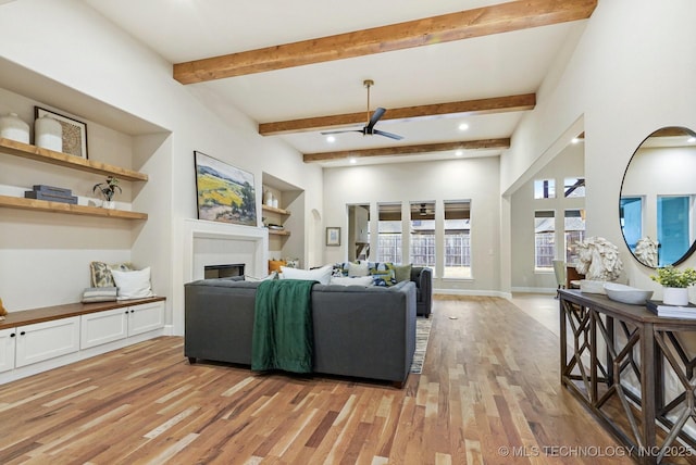 living room featuring ceiling fan, built in features, beamed ceiling, and light hardwood / wood-style flooring