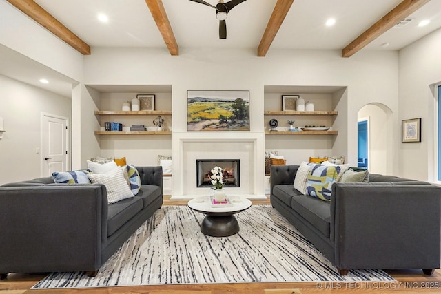 living room with ceiling fan, light wood-type flooring, and beamed ceiling