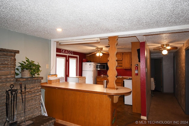 kitchen with kitchen peninsula, a breakfast bar, white appliances, and a textured ceiling