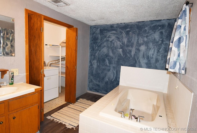 bathroom with vanity, a relaxing tiled tub, a textured ceiling, washer / dryer, and wood-type flooring