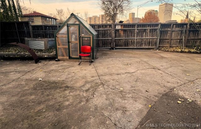 yard at dusk with a greenhouse, a view of city, a gate, fence, and an outdoor structure