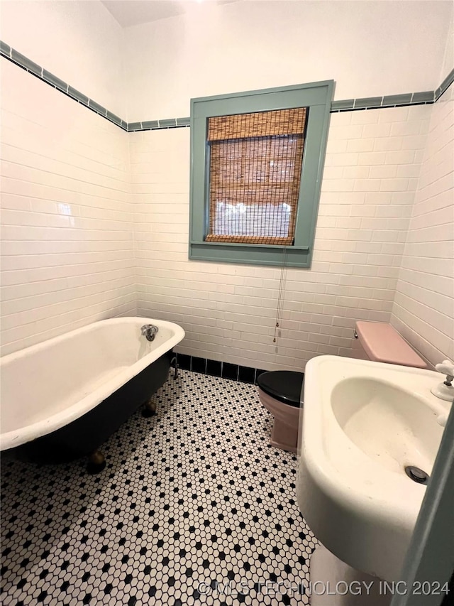 full bathroom featuring tile walls, toilet, a soaking tub, tile patterned floors, and a sink