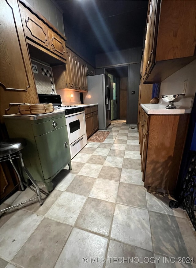 kitchen with white gas range oven, stainless steel refrigerator with ice dispenser, and light countertops